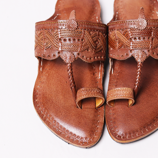 Pair of brown sandals with intricate designs on a white background