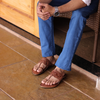 Person wearing brown sandals and blue jeans sitting on a wooden bench.