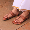 Brown sandals worn on feet with a white garment featuring orange trim.