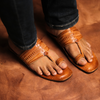 Brown leather sandals worn with blue jeans on a brown surface