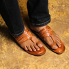 Brown leather sandals worn with rolled-up jeans on a textured surface