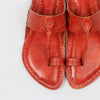 Pair of red leather sandals with intricate designs on a light gray background