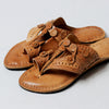 Pair of tan sandals with intricate designs on a light gray background
